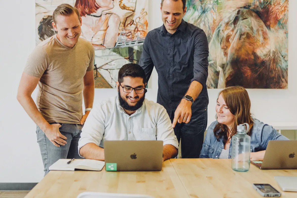 Four colleagues smiling around a laptop