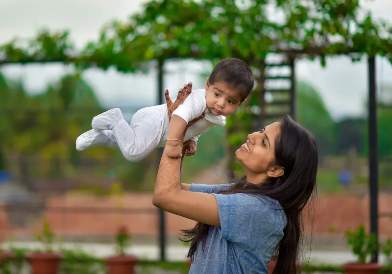 A mother lifting her baby into the air outdoors